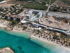 Eine Luftaufnahme eines Küstenresorts mit mehreren Gebäuden, einem Strand und einem Schwimmbad.