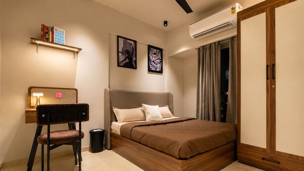 Un dormitorio con cama, escritorio, silla, basurero y unidad de aire acondicionado.