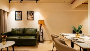 Una sala de estar moderna con un sofá de cuero verde, una mesa de comedor con sillas y dos obras de arte colgadas en la pared.