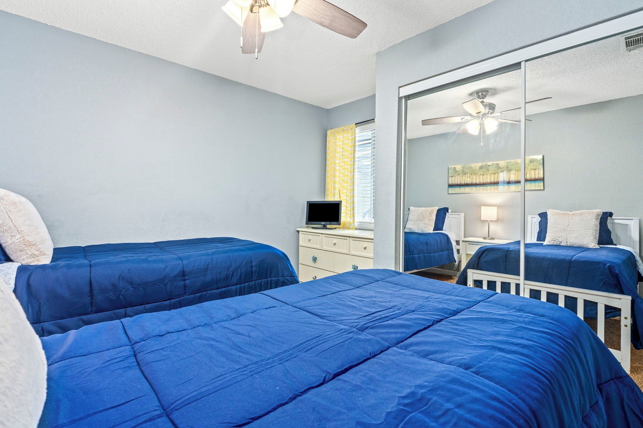 Une chambre avec deux lits, une commode, un téléviseur et un ventilateur de plafond.