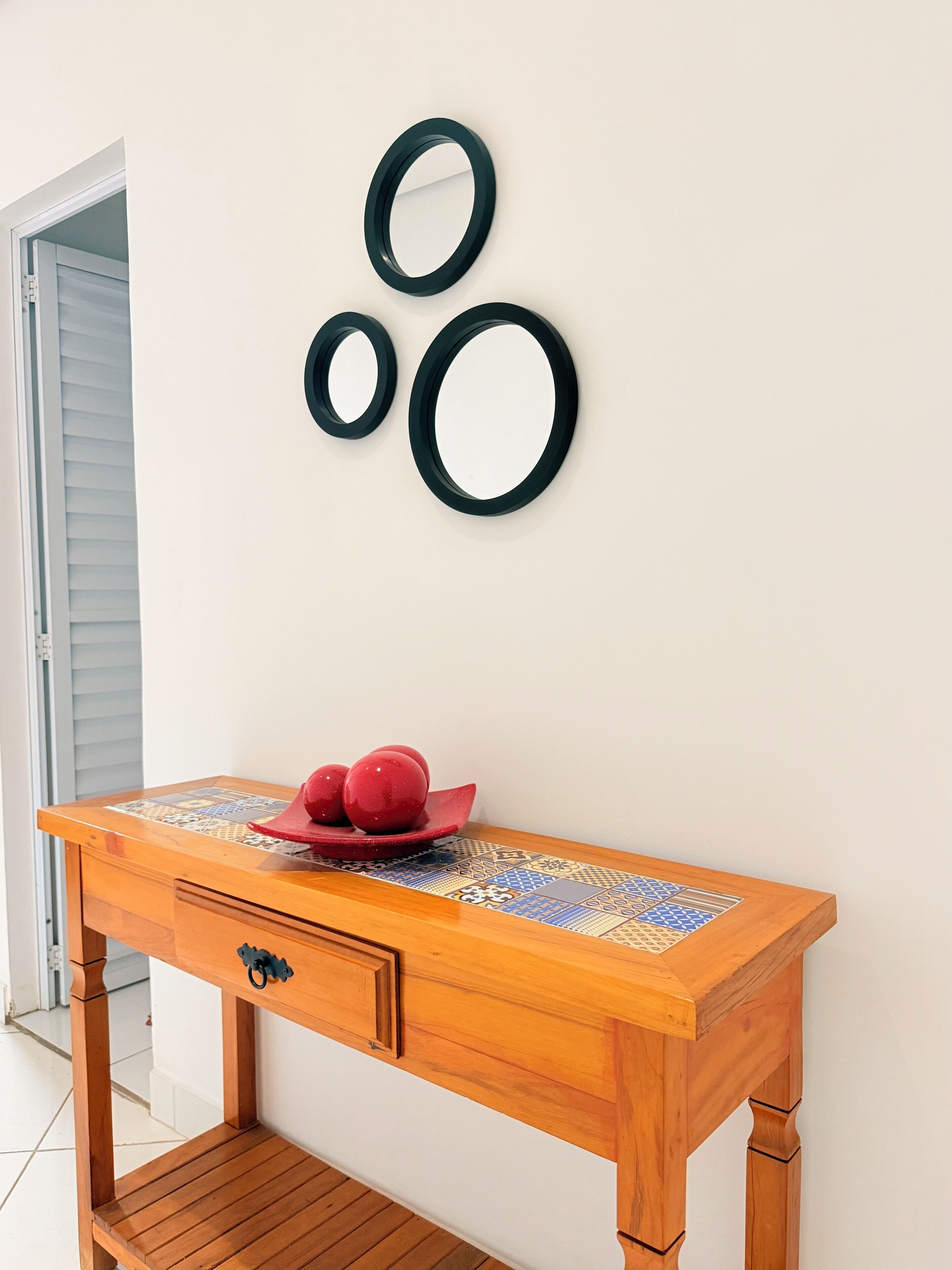 Um console de madeira com tampo estampado, uma gaveta e um prato decorativo com objetos esféricos vermelhos.