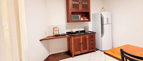 A compact kitchen with a wooden cabinet, a microwave, a refrigerator, and a dining table with chairs.