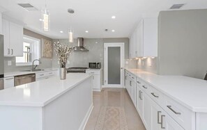 A modern kitchen with white cabinetry, a central island, pendant lighting, and a stainless steel range hood. - Private Retreat • Pool • Jacuzzi • Mini Golf (Pinellas County)