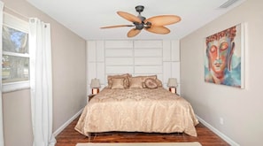 A bedroom with a bed, ceiling fan, artwork, and nightstands. - Heated Pool • Jacuzzi-Fire Pit - Mini Golf - Game (Pinellas County)