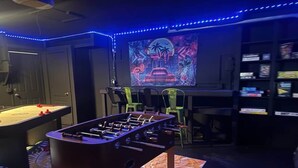 Ein Zimmer mit Tischfußball, Billardtisch und einer neonbeleuchteten Stadtbild-Wandmalerei.