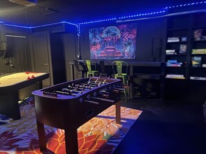A room with a foosball table, a pool table, and a neon-lit cityscape mural on the wall. - Private Retreat • Pool • Jacuzzi • Mini Golf (Pinellas County)