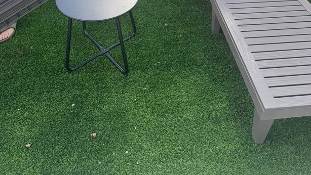 Eine Terrassenfläche mit einem kleinen runden Tisch und zwei Lounge-Stühlen, einer davon mit einem rosa Kissen.