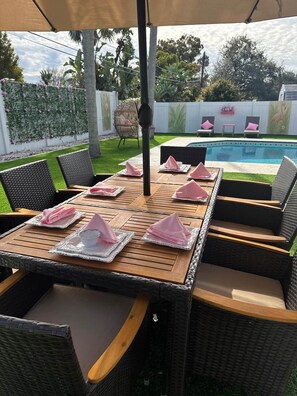 An outdoor dining area with a pool in the background. - Heated Pool • Jacuzzi-Fire Pit - Mini Golf - Game (Pinellas County)