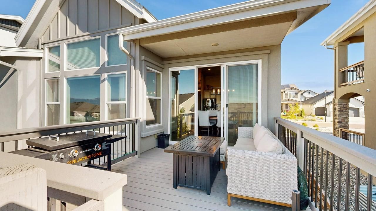 A covered outdoor deck with a barbecue grill, a seating area with a sofa and a table, and a view of the neighborhood.