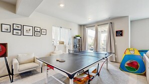 A room with a ping pong table, a sofa, a bookshelf, and a colorful play tent.