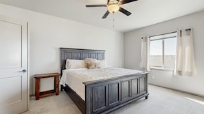 Une chambre à coucher avec un lit, une table de chevet, un ventilateur de plafond, une fenêtre avec des rideaux et une porte.