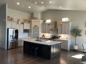 A modern kitchen with a central island, stainless steel appliances, and a view to the dining area. - Elevated Escape- Spacious 5BR Colorado Springs House with Hot Tub and Mountain Views (Colorado Springs)