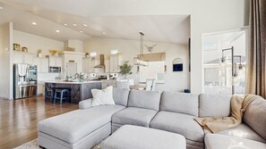 A modern kitchen with white cabinetry, a central island, and a dining area with a light-colored sofa.