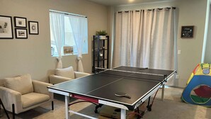 Et bordtennisbord i et rum med en sofa, en reol og et farverigt legetelt.