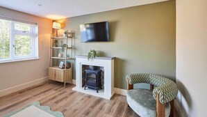 A living room with a fireplace, a television mounted on the wall, a wooden floor, and a chair with a patterned cushion. - Host Stay Sandmoor (Whitby)