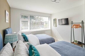 A bedroom with a bed, pillows, a bedside table, a lamp, a window with blinds, a radiator, a TV on the wall, and a clothes drying rack. - Host Stay Sandmoor (Whitby)