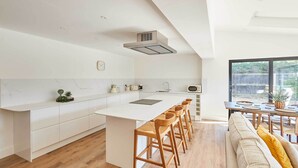 A modern kitchen with a central island, bar stools, and a dining area with a large window. - Host Stay Sandmoor (Whitby)