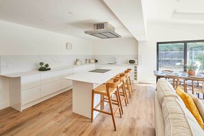 A modern kitchen with a central island, bar stools, and a dining area with a large window. - Host Stay Sandmoor (Whitby)
