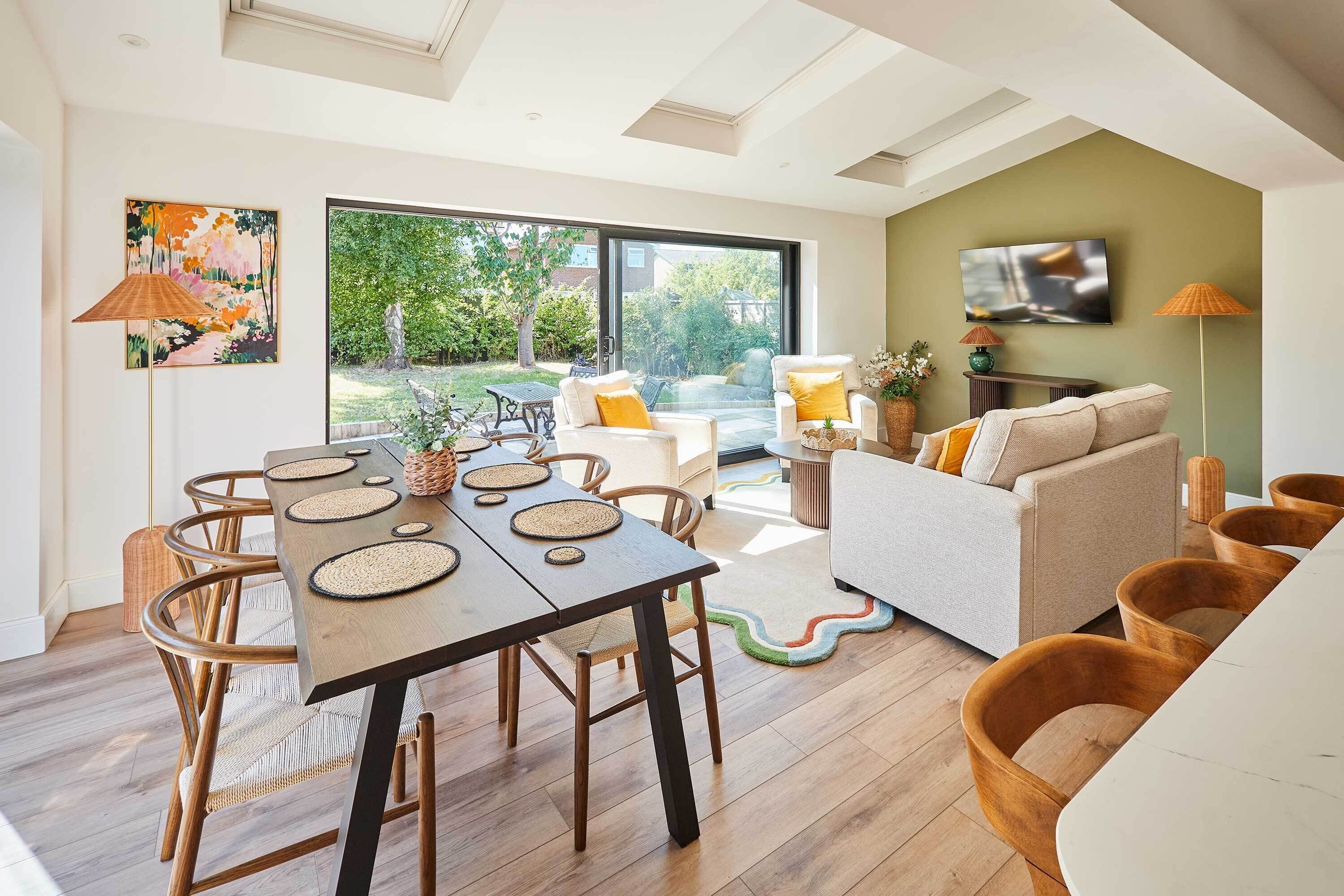 A modern living space with a dining area, a sofa set, and a television mounted on the wall.
