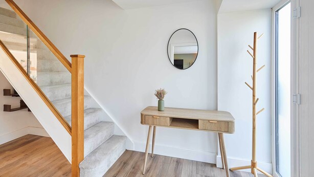 A staircase with wooden handrails, a small console table with a vase, and a coat rack. - Host Stay Sandmoor (Whitby)
