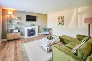 A living room with a fireplace, green sofas, a flat-screen TV, and a bookshelf. - Host Stay Sandmoor (Whitby)