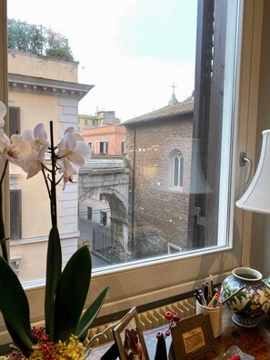 Ein Fenster mit Blick auf eine historische Steinbrücke und Gebäude, eine Vase mit einer Figur sowie ein Schreibtisch mit Bilderrahmen und Stiften.