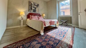 A bedroom with a bed, two bedside lamps, a chandelier, a large window, and a door. - Chic Rome Apartment Master Bonus Study Bedroom (Rome)
