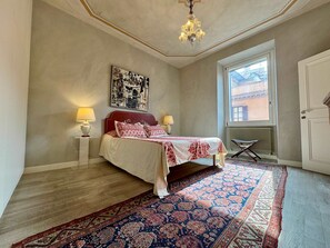 Ein Schlafzimmer mit einem Bett, zwei Nachttischlampen, einer Kandelaberleuchte, einem großen Fenster und einer Tür.