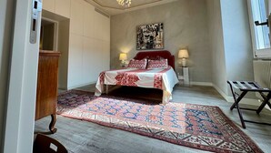 A bedroom with a bed, two bedside tables with lamps, a patterned rug, a wooden cabinet, and a radiator. - Chic Rome Apartment Master Bonus Study Bedroom (Rome)