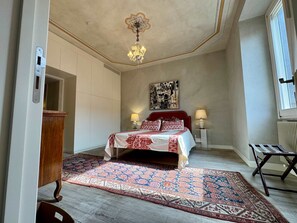 Ein Schlafzimmer mit einem Bett, zwei Nachttischen mit Lampen, einem gemusterten Teppich, einem Holzschrank und einer Heizung.