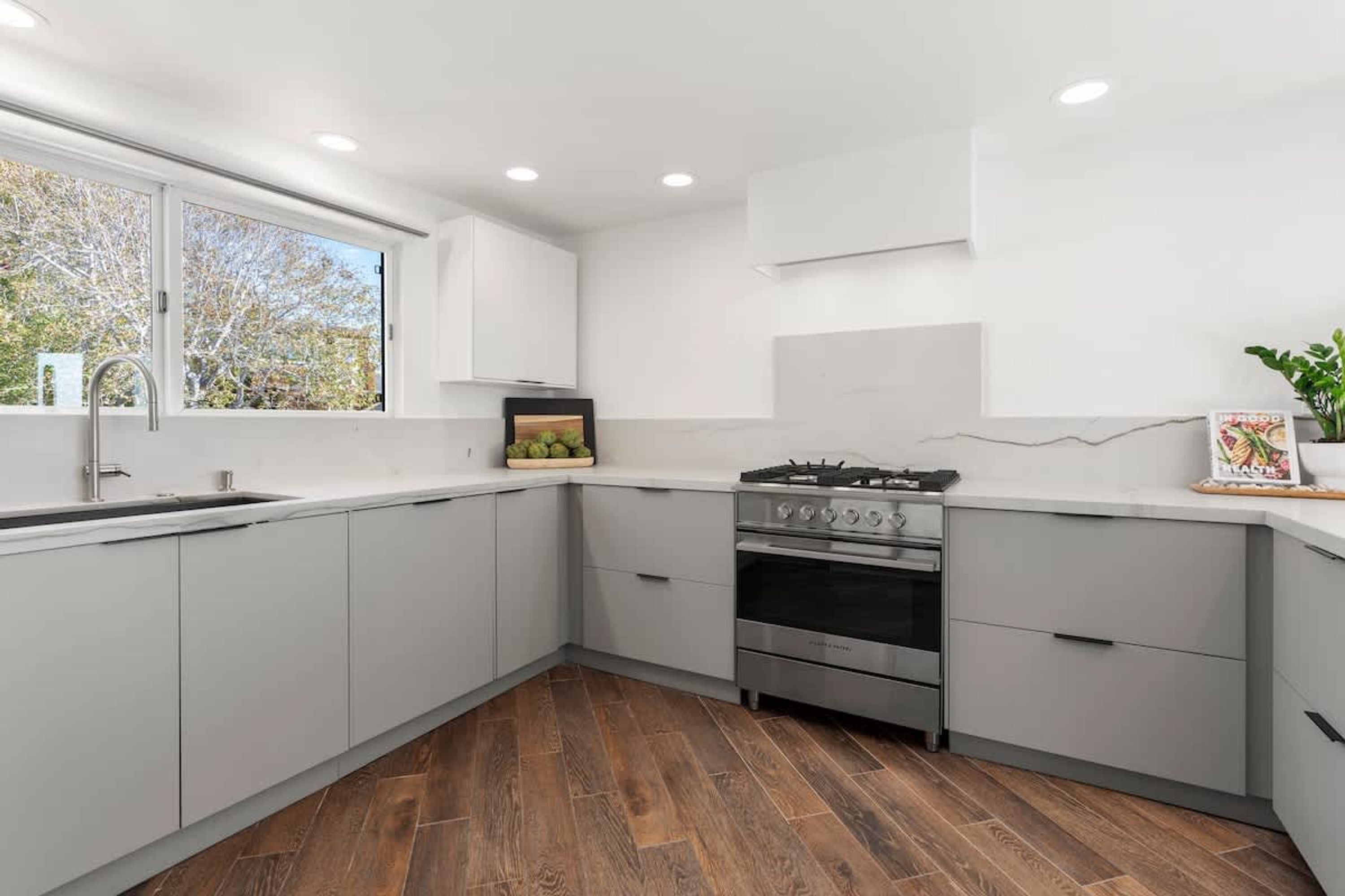 Una cocina moderna con armarios blancos, una estufa de acero inoxidable y una ventana con vistas a árboles.