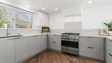Una cocina moderna con armarios blancos, una estufa de acero inoxidable y una ventana con vistas a árboles.