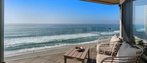 A balcony with a view of the ocean, a table, and two chairs.