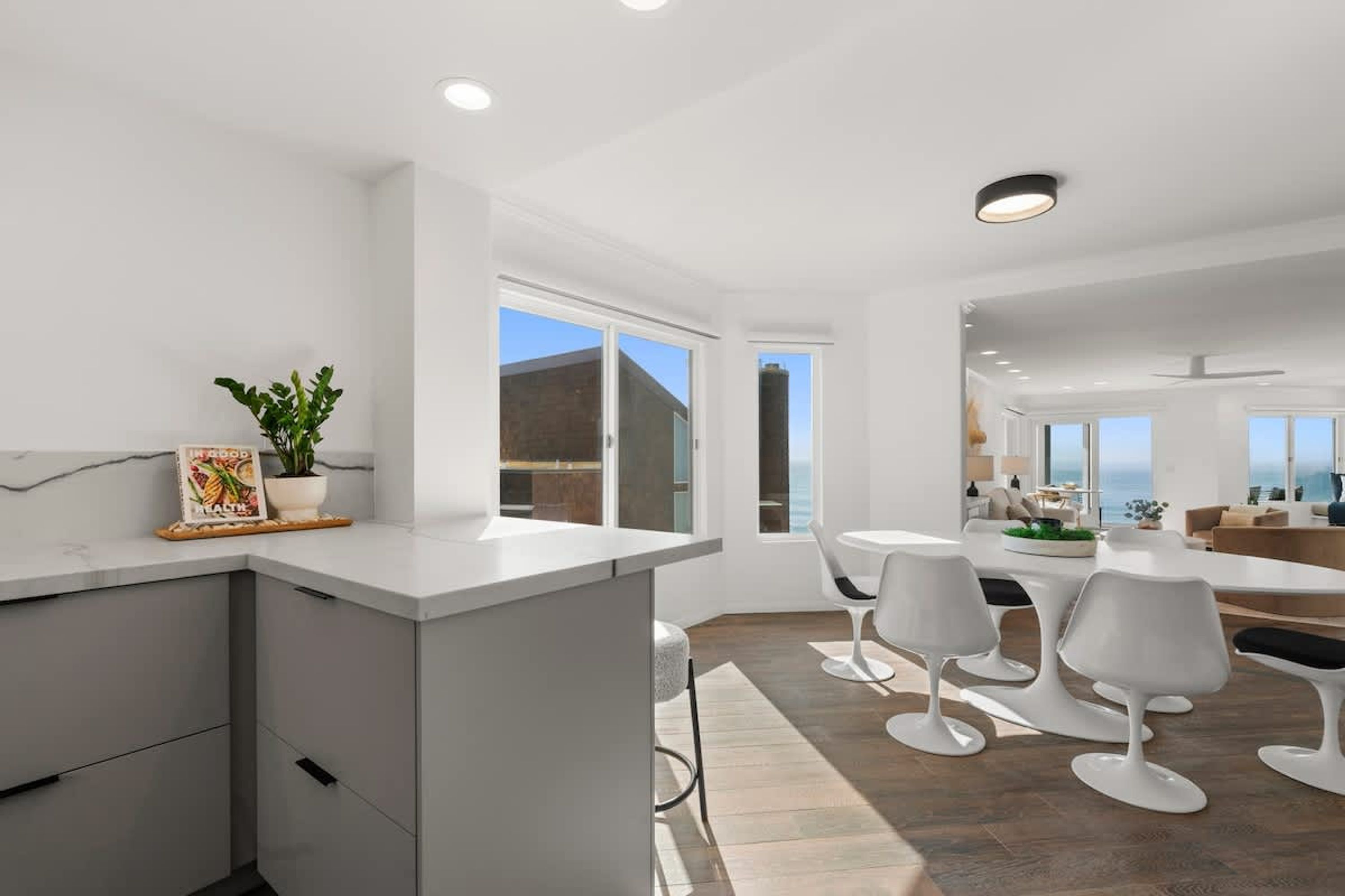 Une cuisine moderne dotée d’un îlot central, de meubles blancs et d’un coin repas avec des chaises blanches.