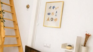 A modern living room with a TV on a wooden stand, a white shelf unit with decorative items, a wooden ladder against the wall, and a framed picture on the wall. - The Magical Village - 5 minutes from the beach (Calonge)