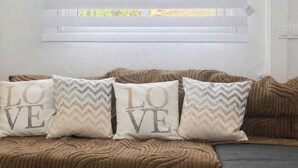 A room with a window covered by blinds, a brown textured sofa, and three pillows with 'LOVE' printed on them. - The Magical Village - 5 minutes from the beach (Calonge)