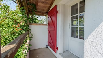 A narrow outdoor corridor with a wooden fence, a red door, and a white wall.