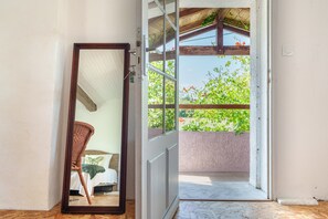 A doorway leading to an outdoor balcony with a view of greenery and a wooden structure overhead.