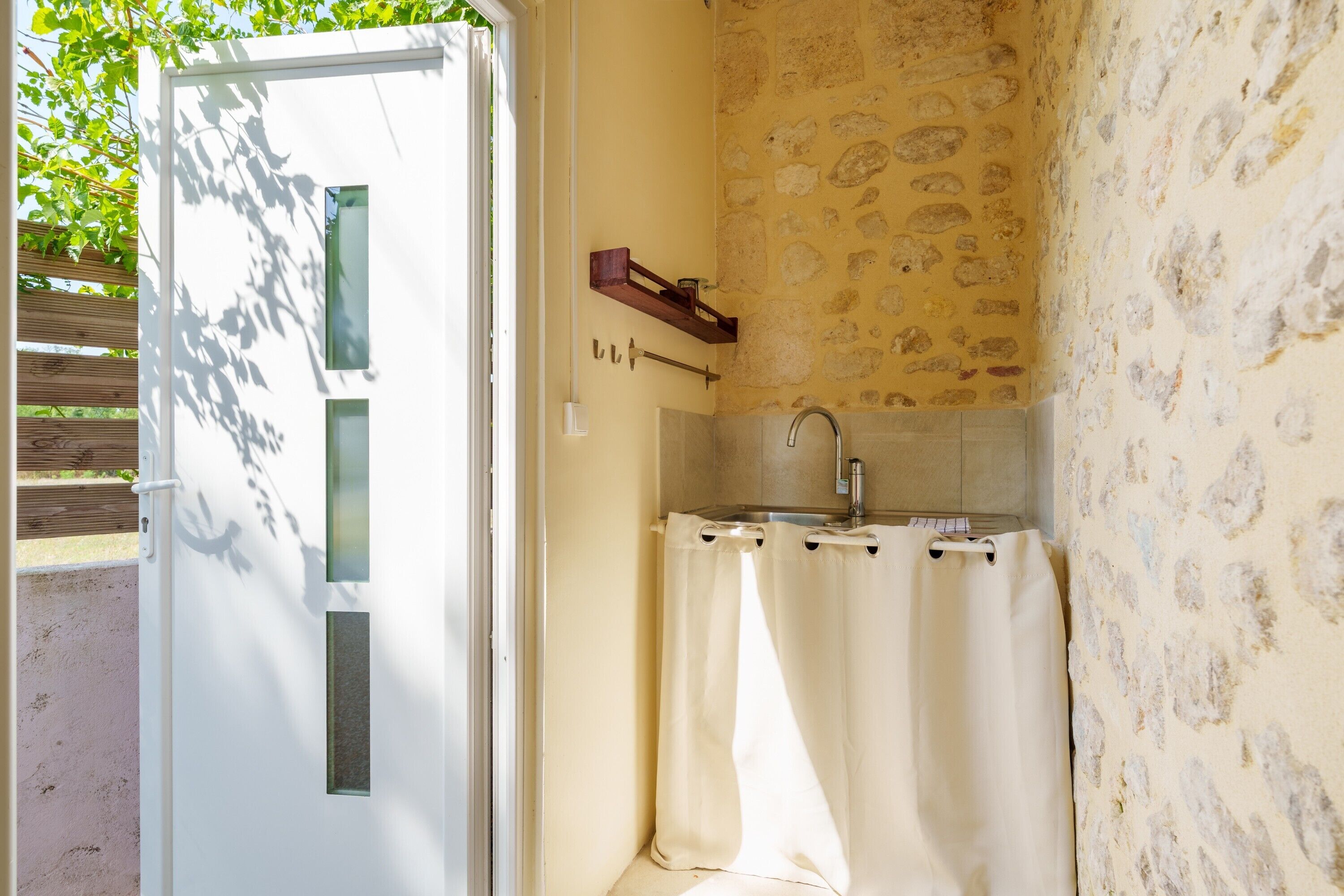 A compact bathroom with a shower curtain, a sink, and a wooden shelf.