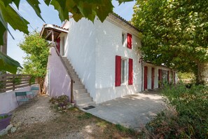 A white building with red shutters, a staircase, and a gravel path leading to a door.