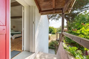 A wooden deck with a view of a garden and a building with a bed and a door.