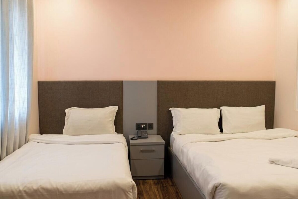 A hotel room with two beds, a nightstand, and a window with curtains.
