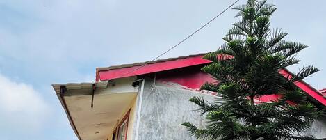 Un edificio con tetto rosso, facciata in cemento e un piccolo albero di fronte.