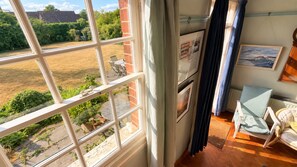 A room with a large window, a dining area, and a view of a garden. - Observatory Apt - Historic Bedford Apt With Pool (Bedford)