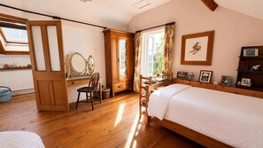 Um quarto com uma cama de madeira, uma escrivaninha com cadeira, um guarda-roupa e uma janela com cortinas.