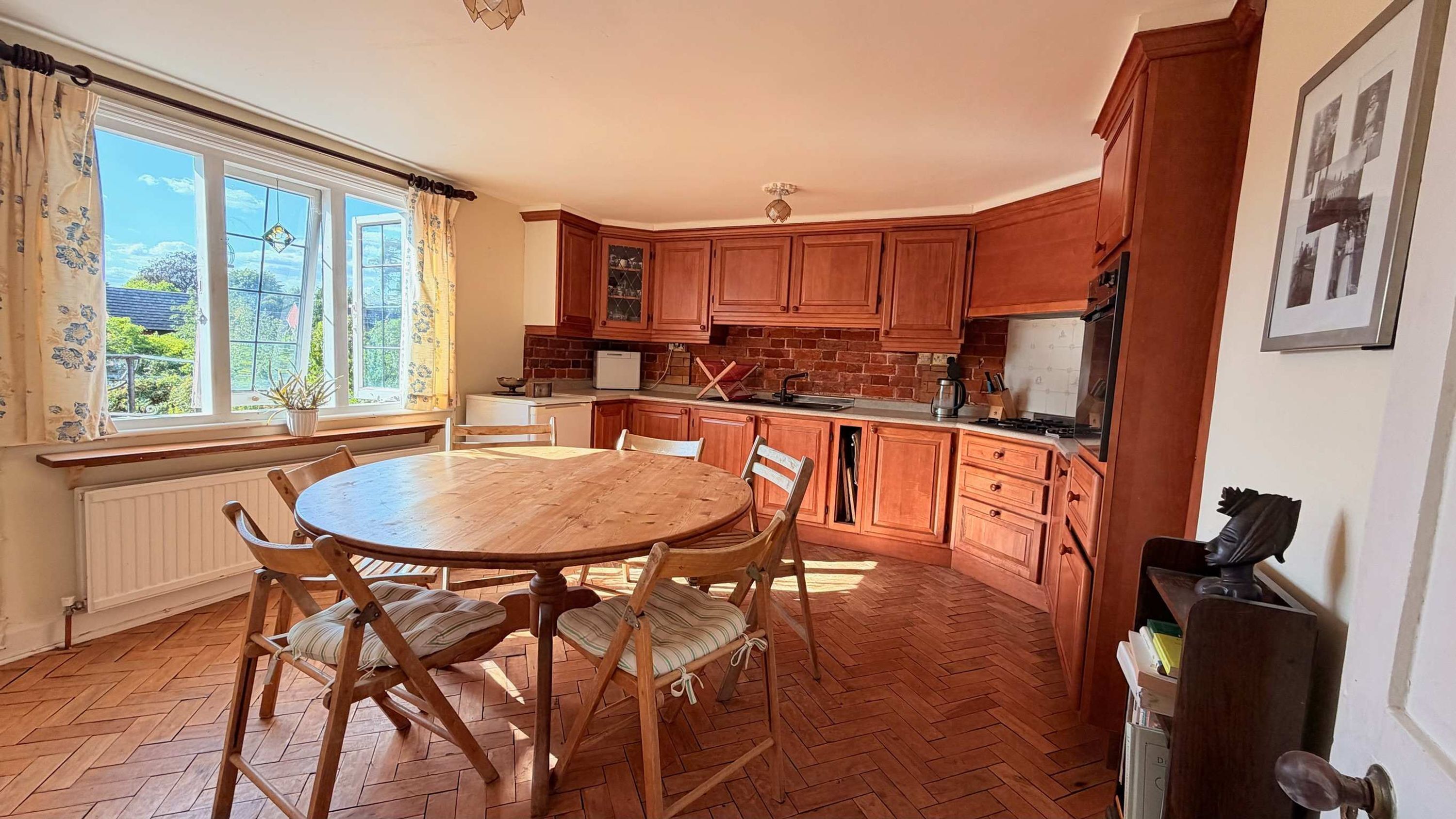 A kitchen with wooden cabinets, a dining table with chairs, and a window with curtains.