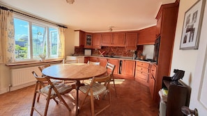 Una cocina con gabinetes de madera, una mesa de comedor con sillas y un ventanal con cortinas.