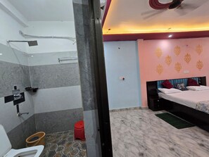 A hotel room with a shower, a bed with decorative pillows, a small stool, and a bucket. - VIP Inn (Ayodhya)