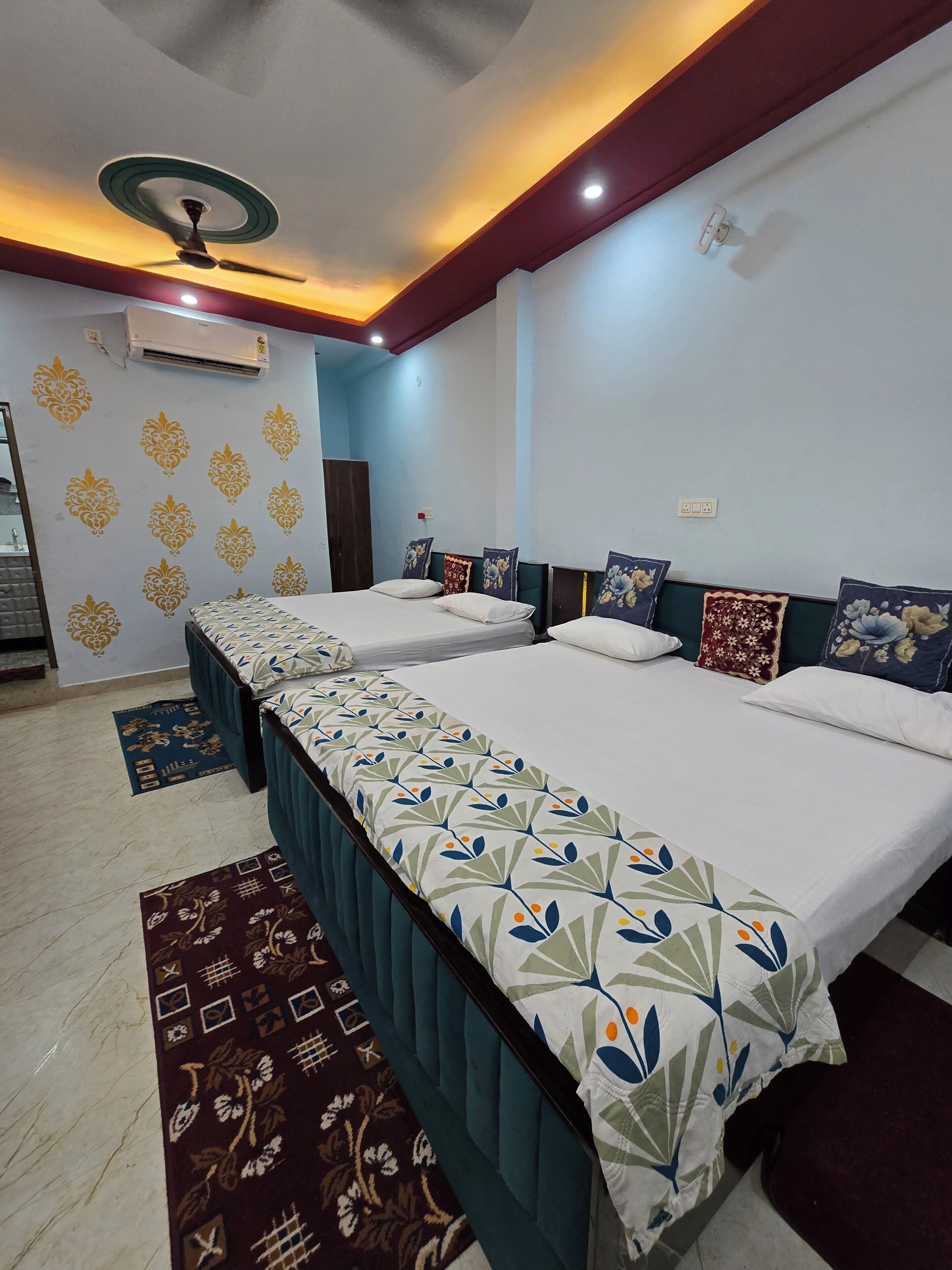 A hotel room with three beds, a ceiling fan, an air conditioning unit, and a patterned rug.