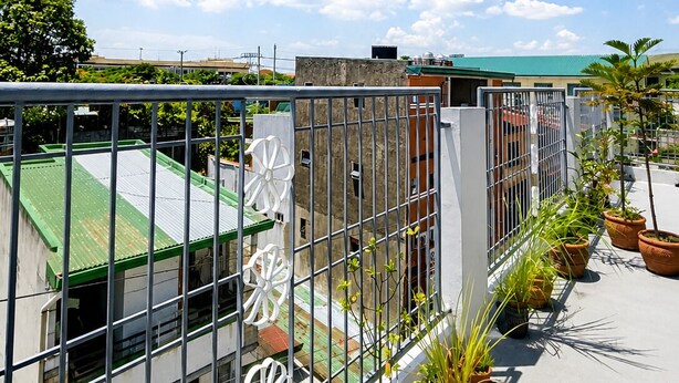 Una terraza con barandilla de metal, plantas en macetas y edificios al fondo.